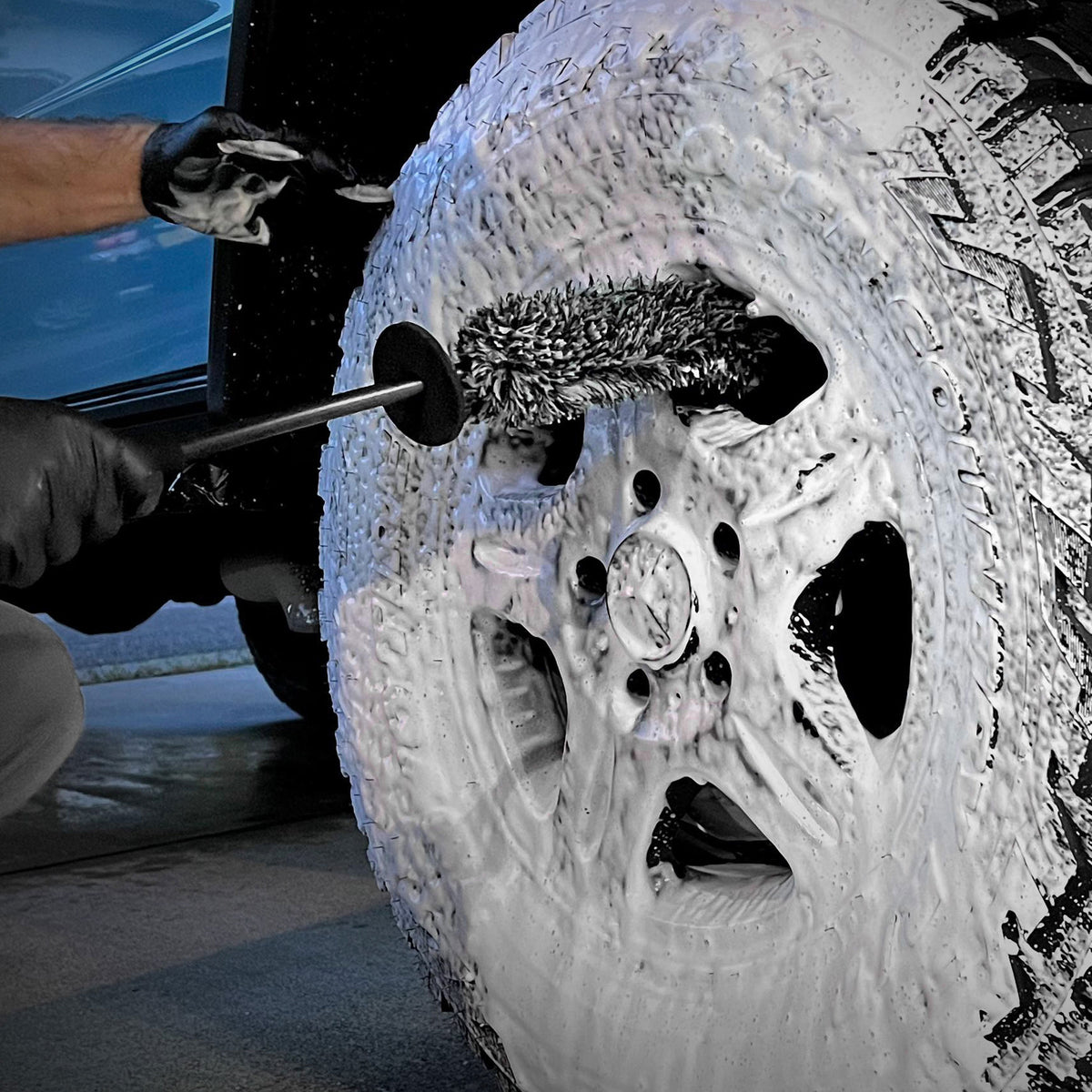  Detailer utilizza CARPRO Flat & Spot Brush per pulire accuratamente il cerchione di un'auto coperto di schiuma.