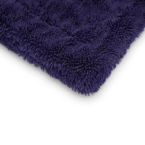 Dettaglio angolare di un panno in microfibra blu scuro, assorbente, ideale per un'asciugatura delicata e priva di aloni delle superfici auto.